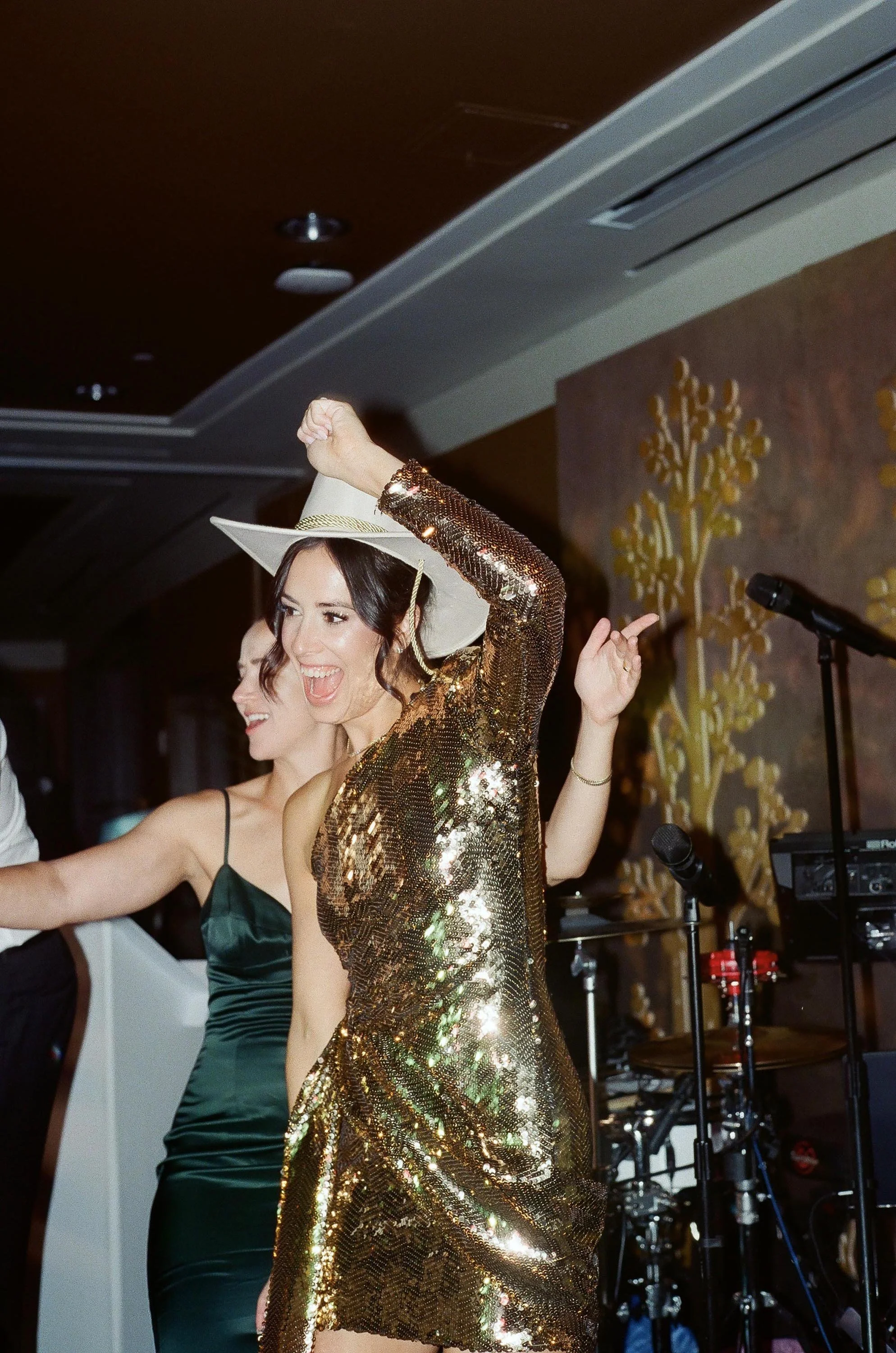 a bride wearing a cowboy hat and a shimmering dress dancing with friends and family