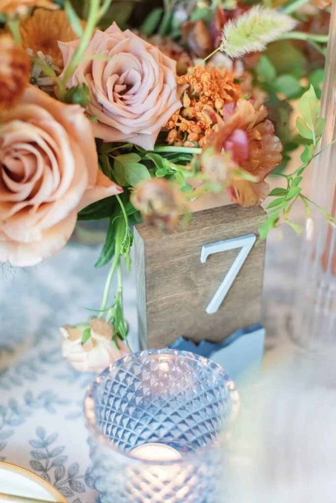 2026 wedding design trend with romantic florals, wood table number, and cut-glass votive candlelight.