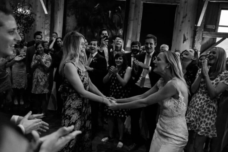 Bride and guest share a joyful dance surrounded by cheering guests, highlighting the wedding guest experience.