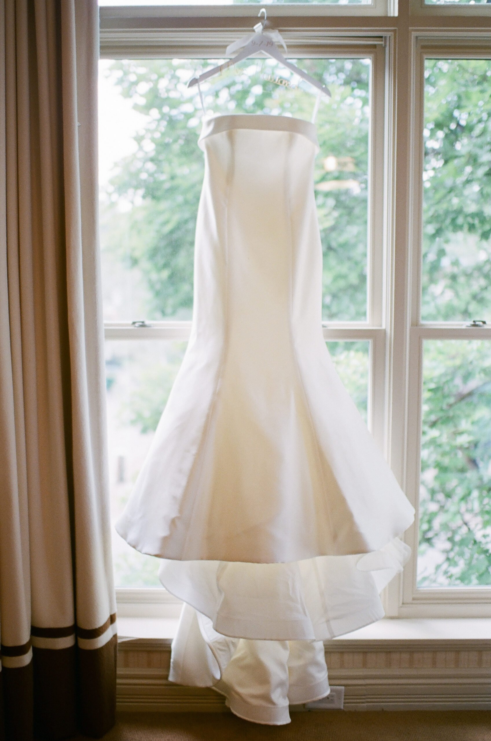 the brides white gown hanging in the window