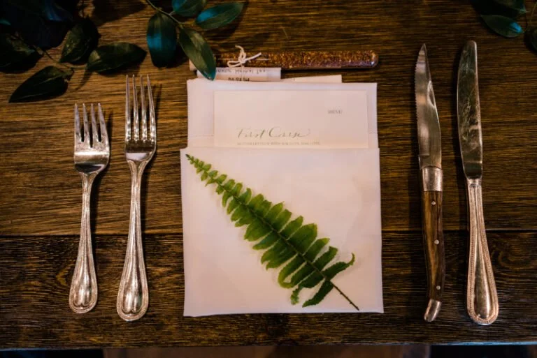 Nature-inspired wedding place setting with fern, menu, and vintage flatware to elevate the guest experience.