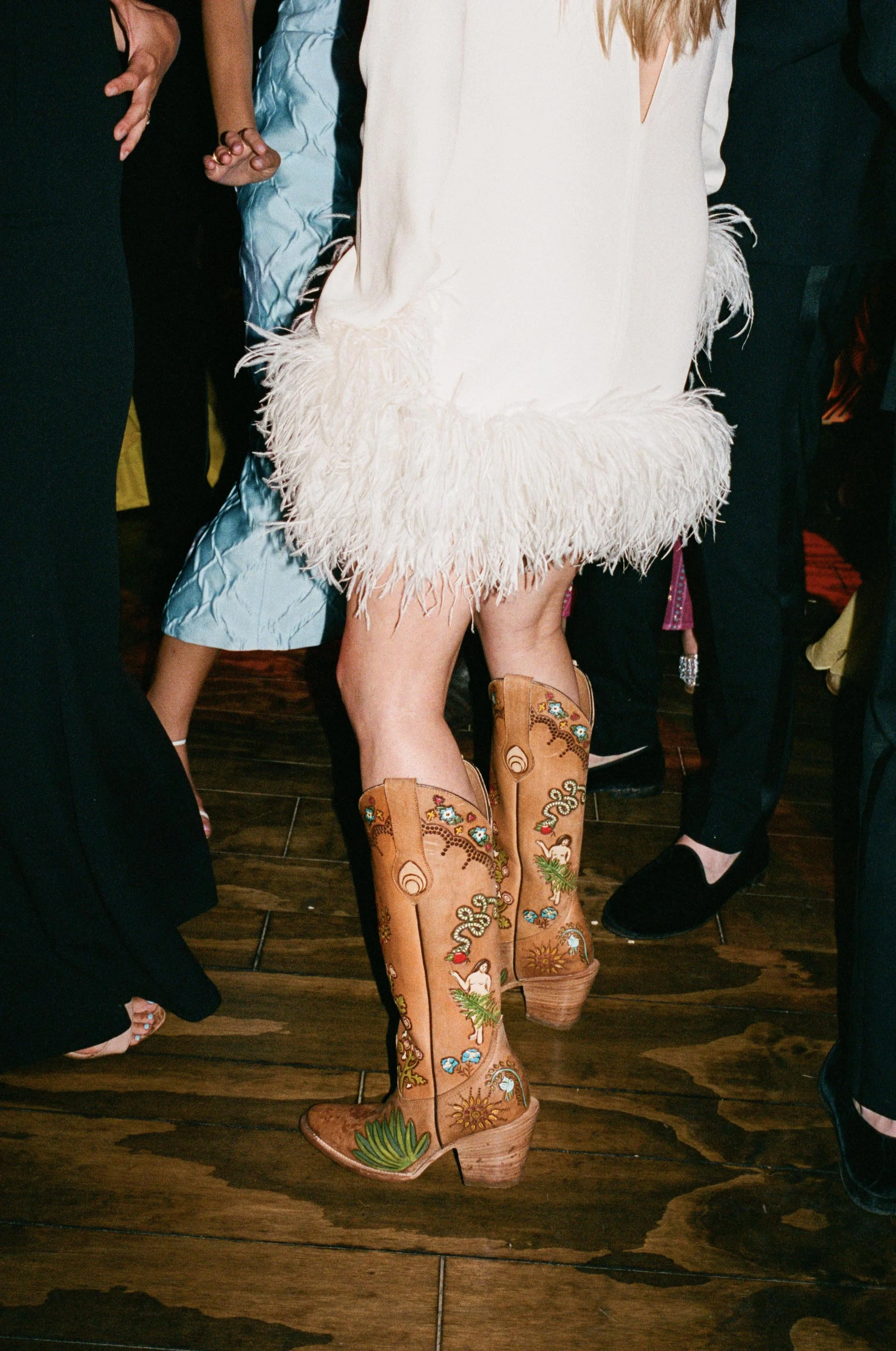 a bride dancing after her wedding wearing a white feathered dress and embroidered cowboy boots
