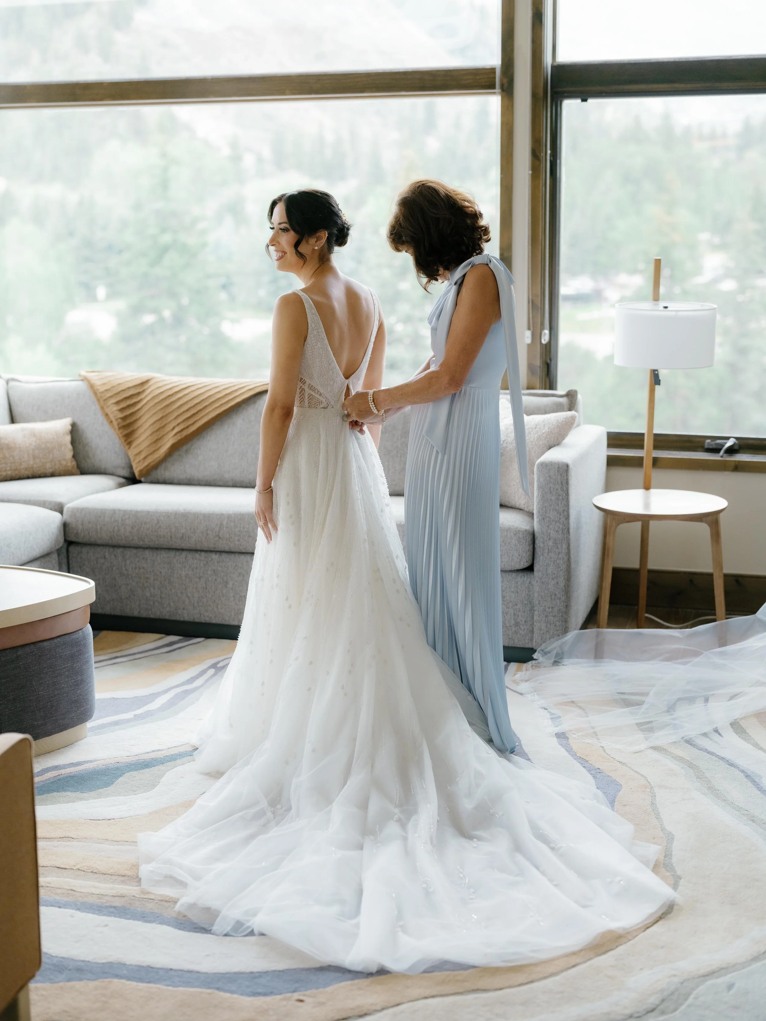 a mother of the bride helping her daughter put her wedding dress on