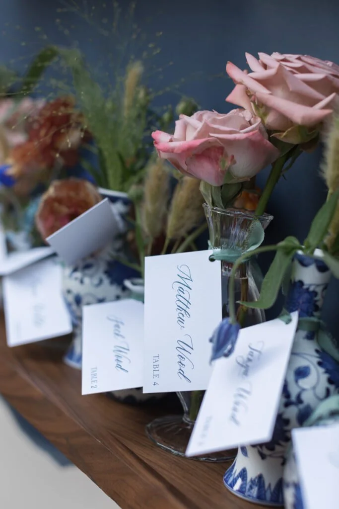 Escort cards displayed in blue-and-white bud vases with florals at a luxury fall wedding.