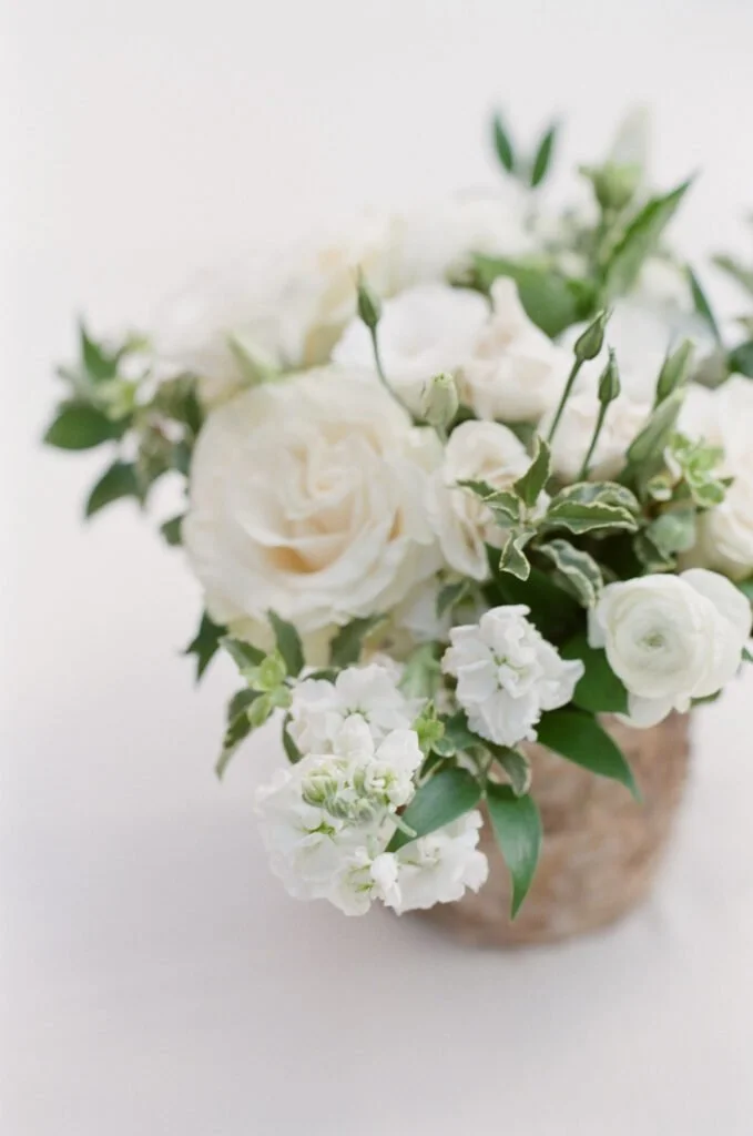 Soft white floral arrangement with roses, ranunculus, and greenery in a textured vase, styled for a wedding at The Cliff House.
