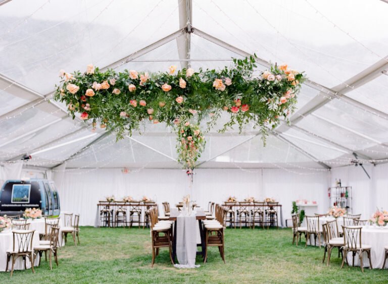 Tent wedding reception with floating floral chandelier, round and long tables, and soft garden-inspired design.