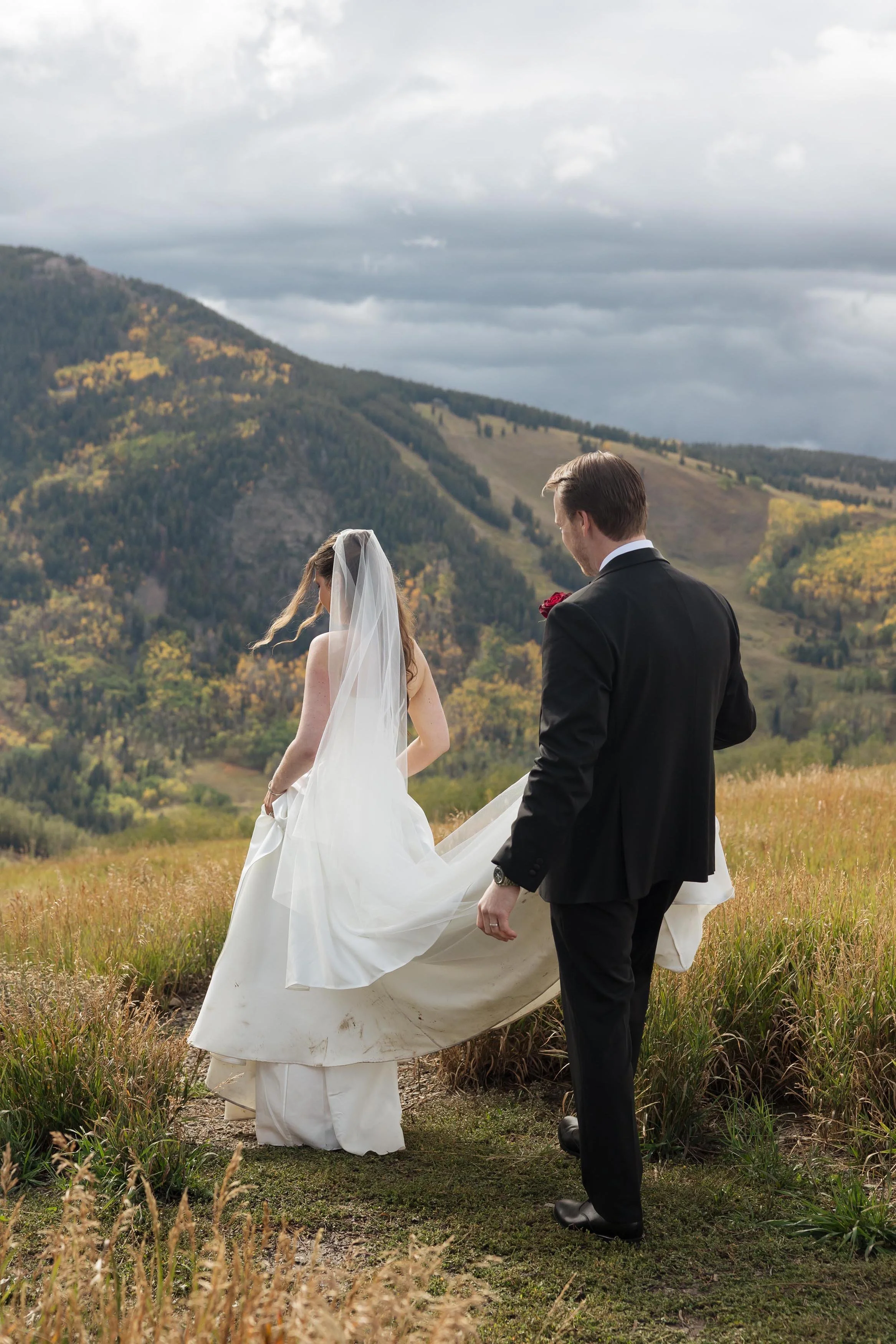 a groom holding his bride's wedding dress up while atop colorado mountains