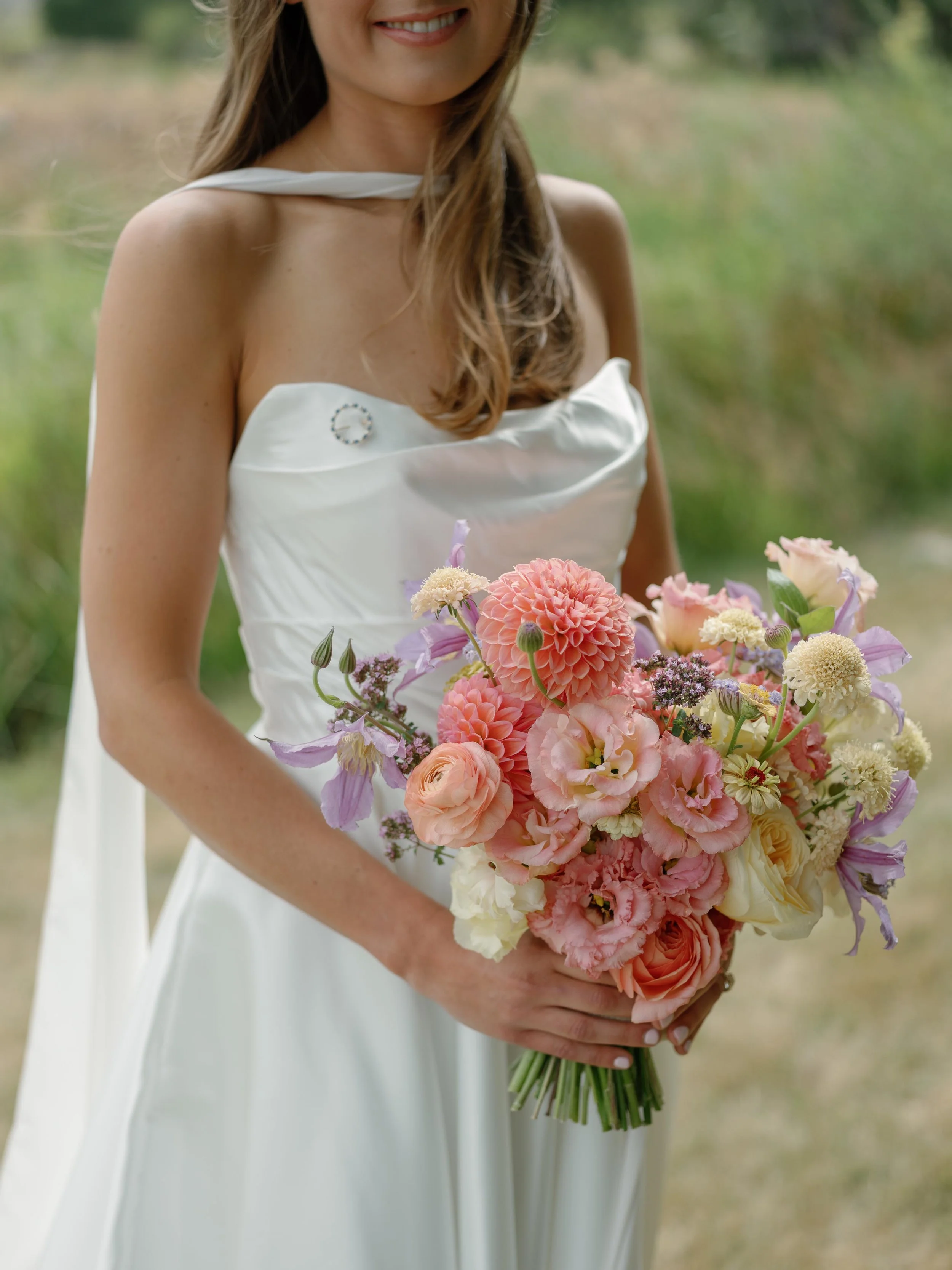 a bride holding a beautiful custom floral arrangement in front of a field in colorado