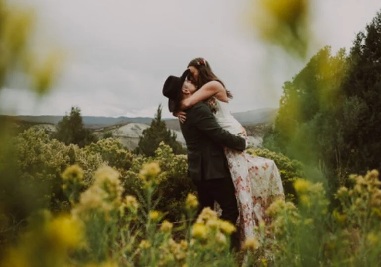 Couple embracing in a wildflower field with mountain views in the background.