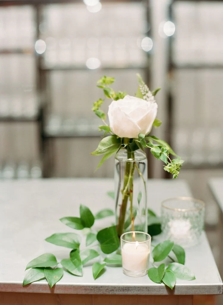 Single stem rose in glass vase with greenery and candle at Cape Cod wedding venue reception table.