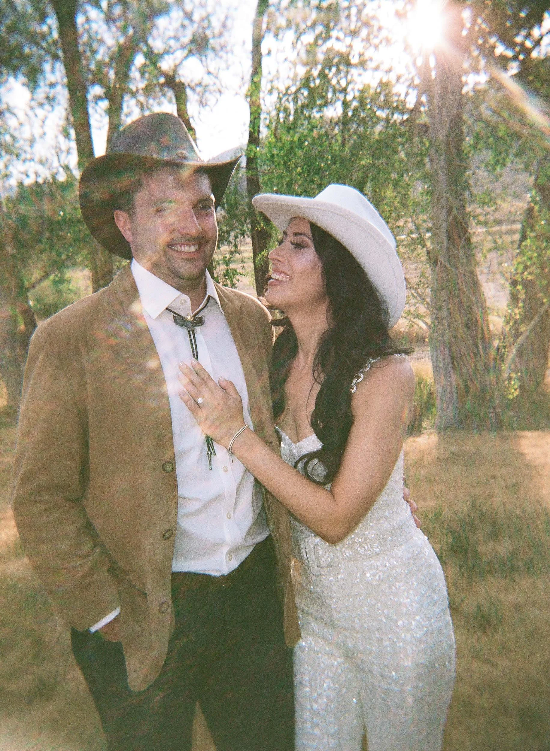 a bride and groom laughing with each other dressed in western attire