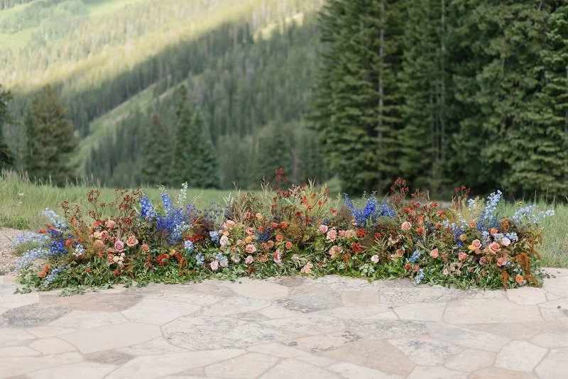 Mountain ceremony florals with colorful wildflower arrangements and lush greenery overlooking a scenic forest landscape.