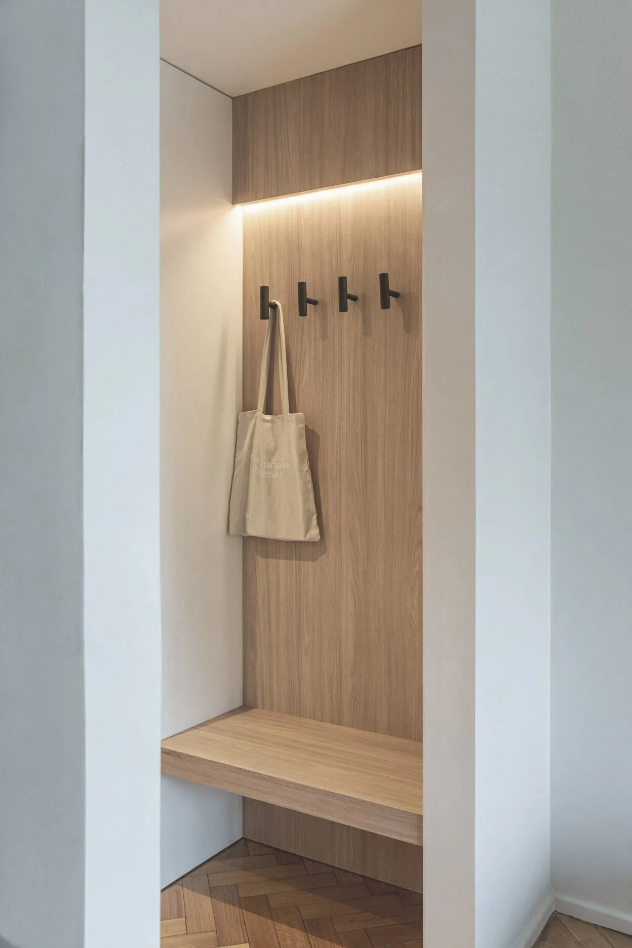 Rincón funcional con panel de madera, ganchos negros y luz LED empotrada — detalle de interiorismo en Buenos Aires