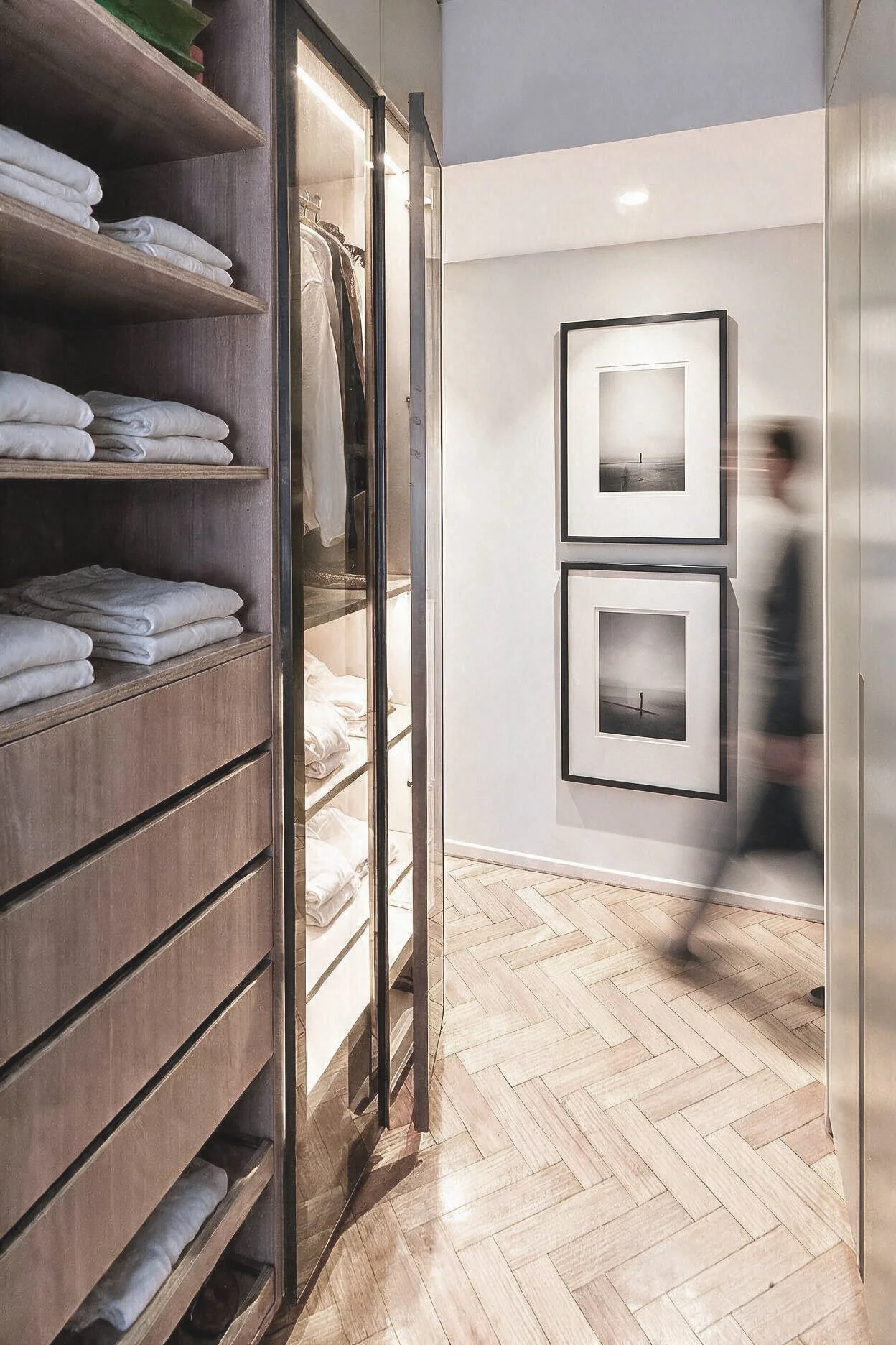 Vestidor con estantería de madera, toallas blancas, placard con frente de vidrio y piso en espiga — proyecto de interiorismo en CABA