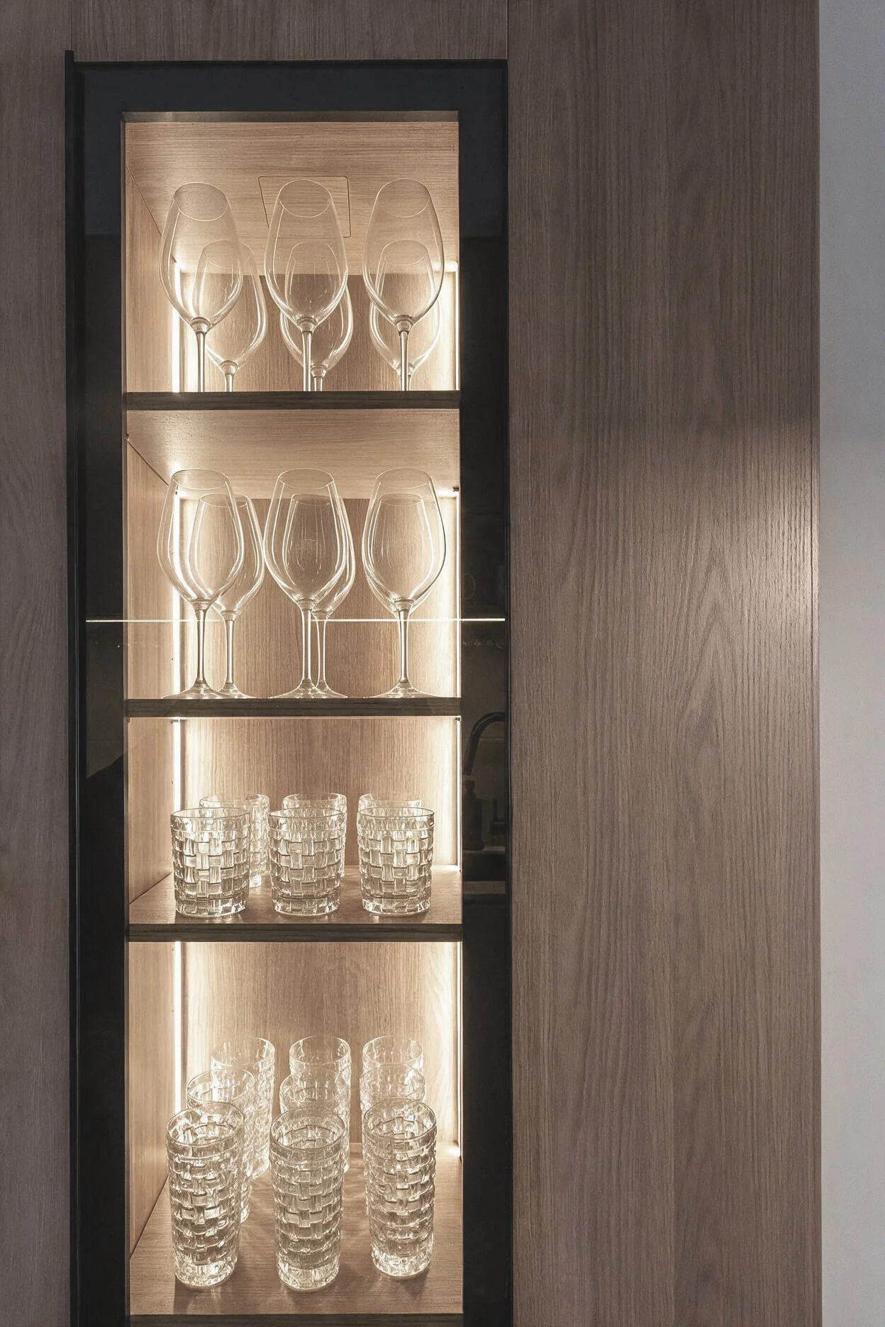Vitrina de cristalería con copas y vasos, iluminación suave y fondo de madera — detalle de interiorismo en CABA