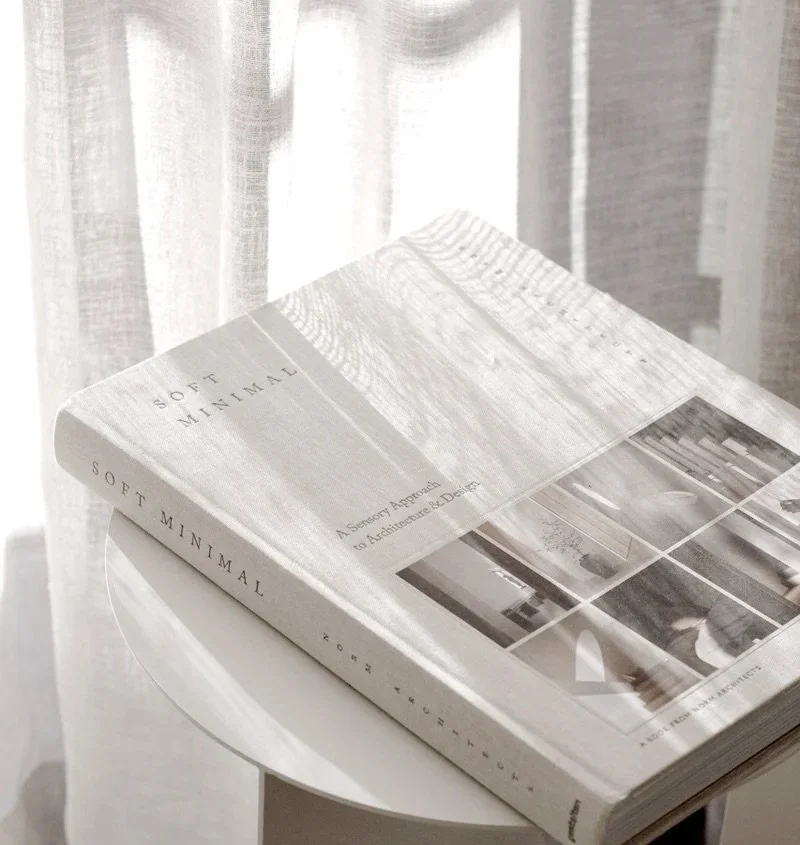 Detalle de living minimalista con libro sobre mesa redonda blanca junto a cortina de gasa — proyecto de interiorismo en Buenos Aires