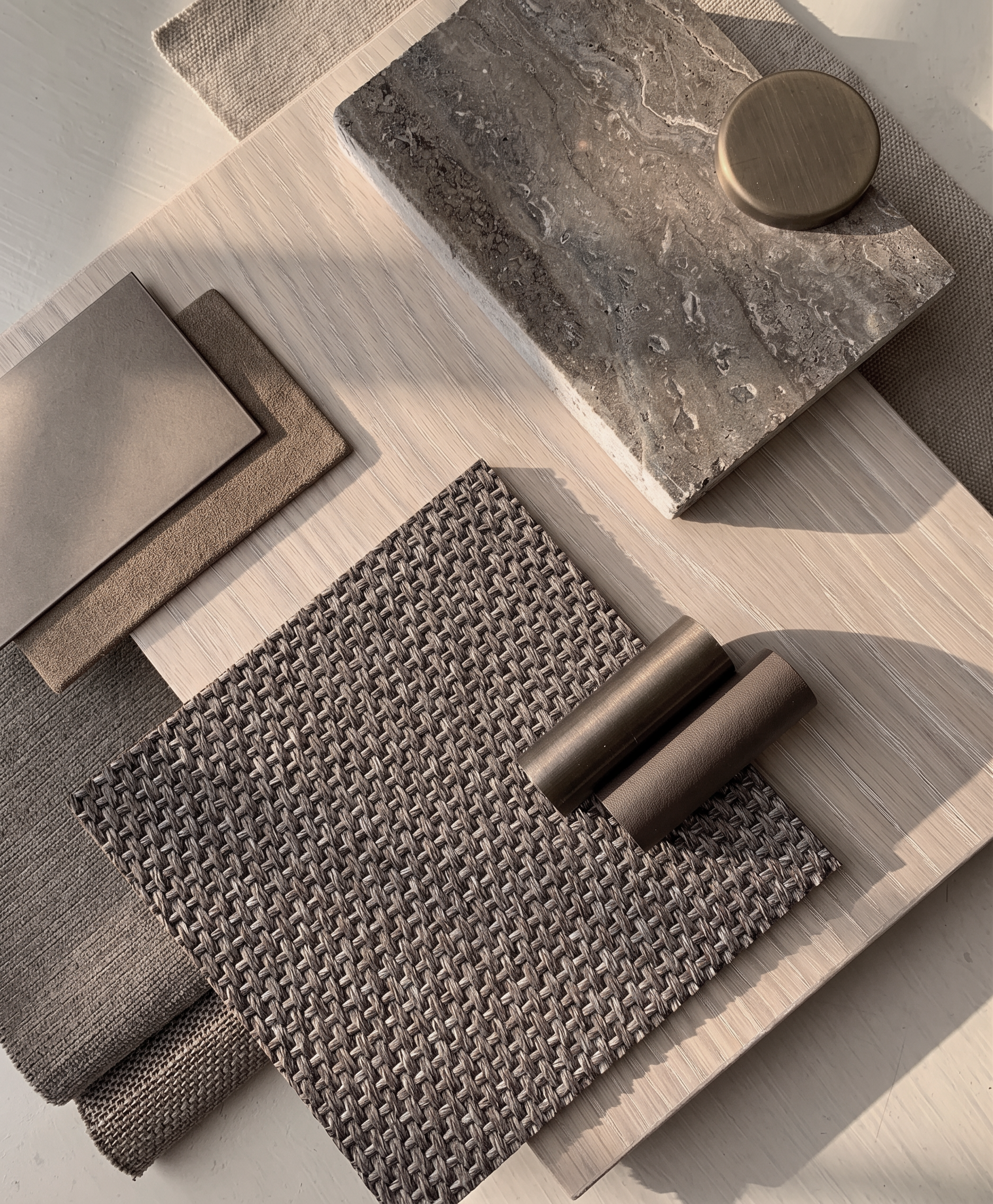 Muestrario de revestimientos y accesorios para decoración interior, incluyendo diferentes muestras de textiles, un red de mimbre, una balda de piedra y objetos decorativos sobre una mesa de madera.
