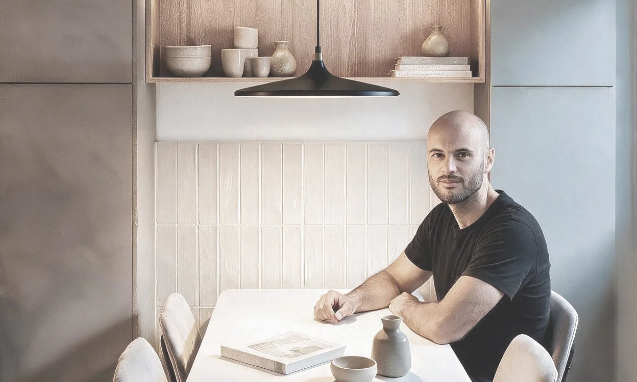 Comedor con mesa blanca, vajilla y objetos decorativos, paredes en madera clara y gris, estantería con cerámica beige y lámpara colgante negra — proyecto de interiorismo en Buenos Aires