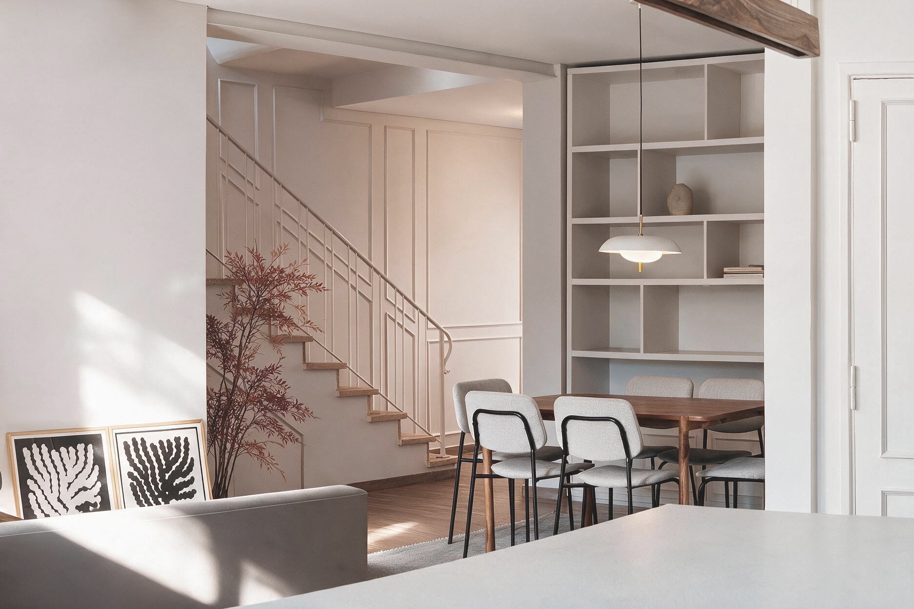 Comedor minimalista con mesa de madera, sillas grises, estantería empotrada blanca y escalera de madera con baranda blanca de fondo — proyecto de reforma en Buenos Aires