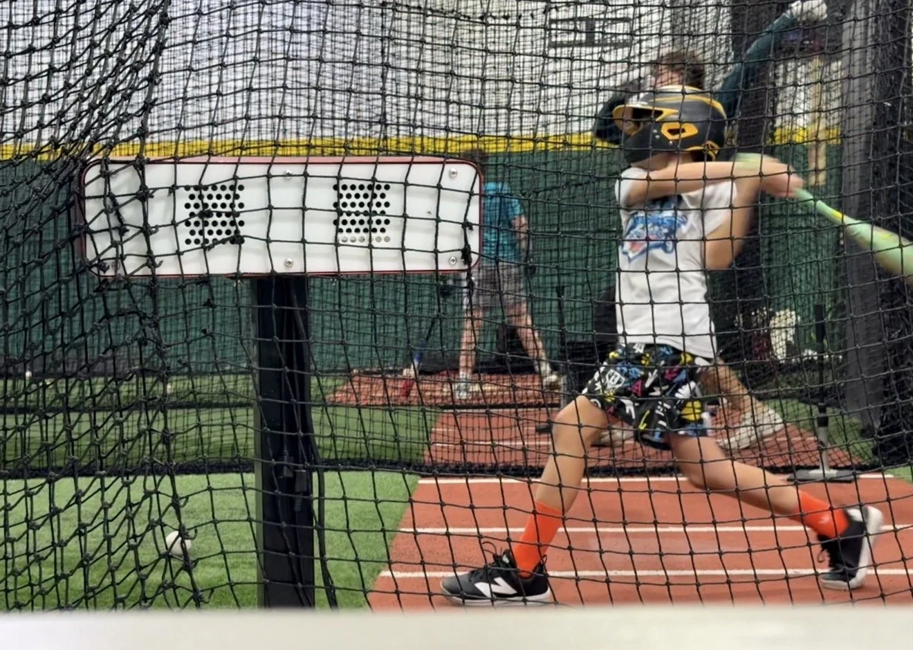 Baseball player taking batting practice inside a training cage at Line Drive Indoor Batting in Jupiter.