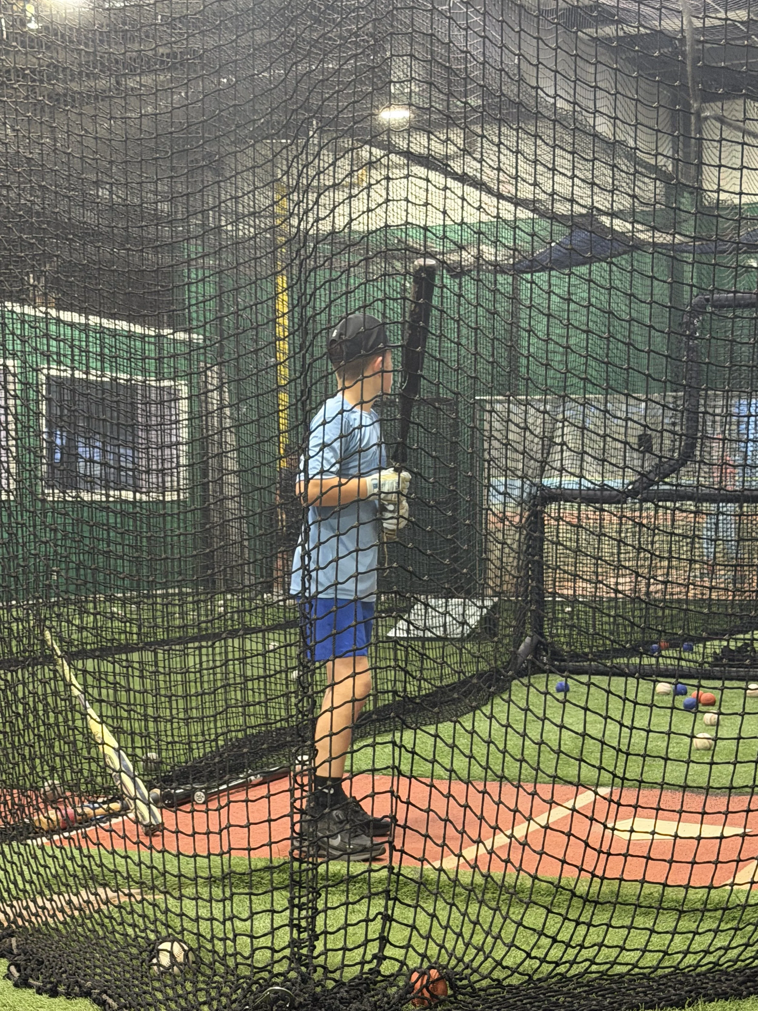 Youth baseball player working with coach Manny Oliveira during private baseball instruction at an indoor batting cage in Jupiter, Florida.