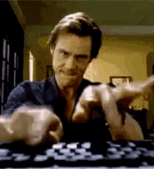 A man in a dark shirt maniacally plays chess with two fluffy dogs, using his hands to move the pieces.