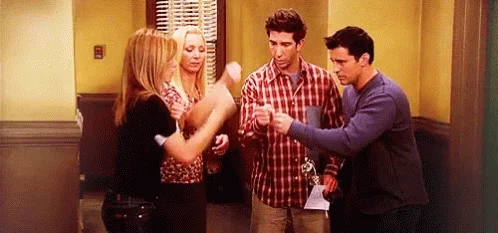 Four people standing in a room, engaging in conversation, one woman raising her hand, others listening.