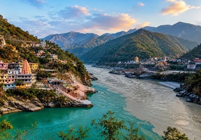 Scenic view of the Ganges River confluence near Devprayag, India, with colorful hillside temples and Himalayan mountains