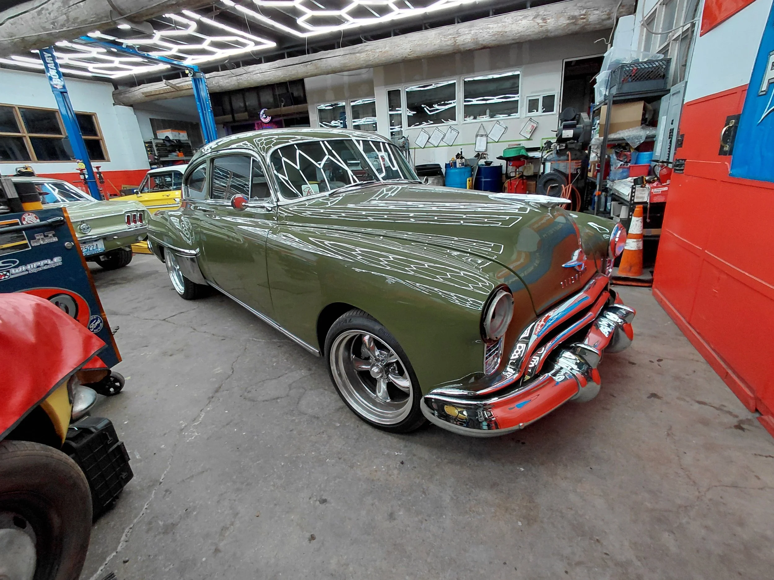 A vintage green car parked inside a garage filled with various tools and equipment.