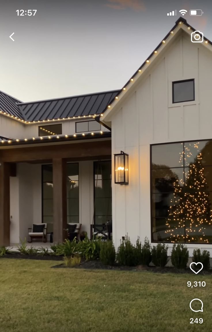 Front view of a modern house decorated with Christmas lights, with a Christmas tree visible through the window.