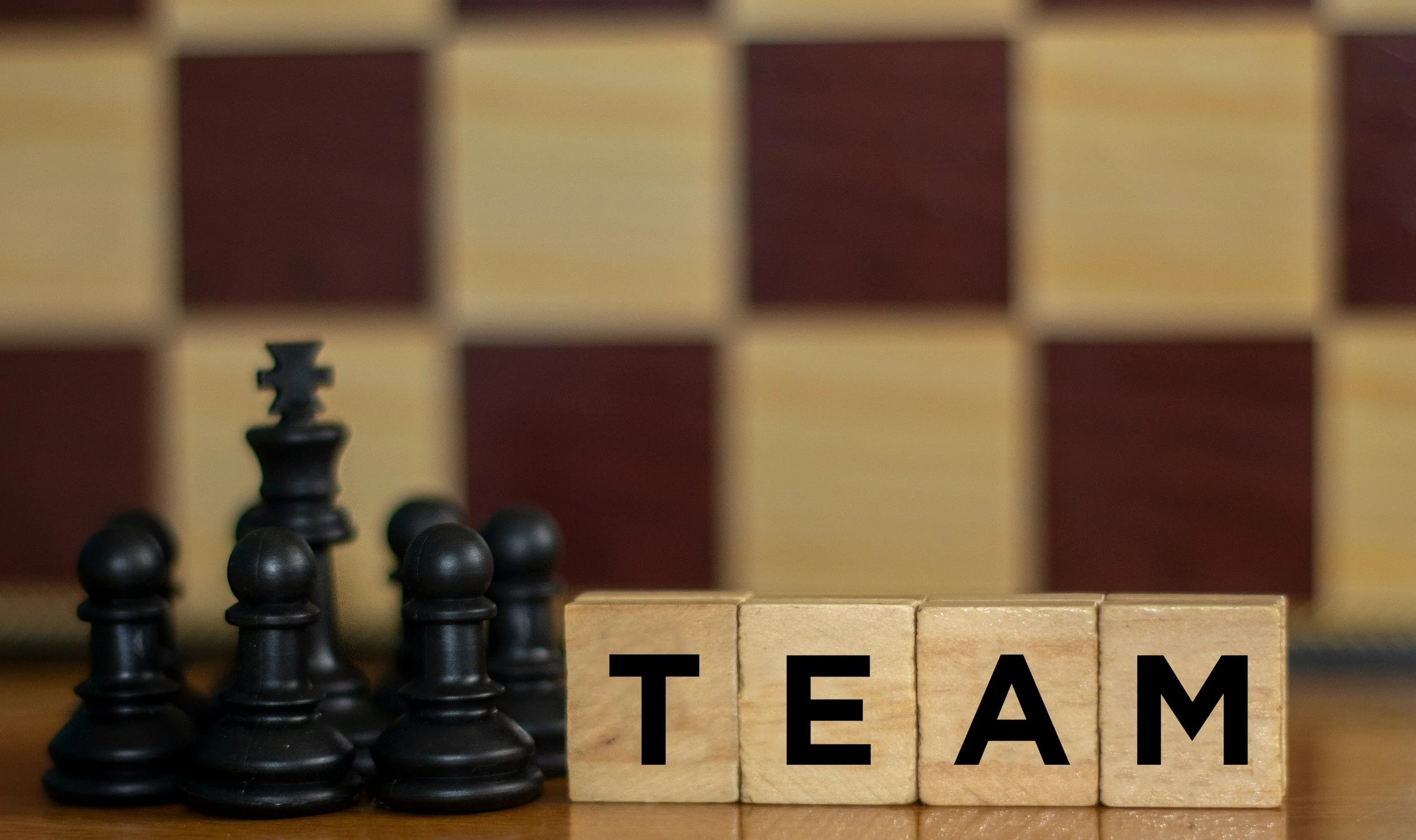 A chessboard with several black chess pieces, and wooden blocks spelling out 'TEAM' at the bottom right.