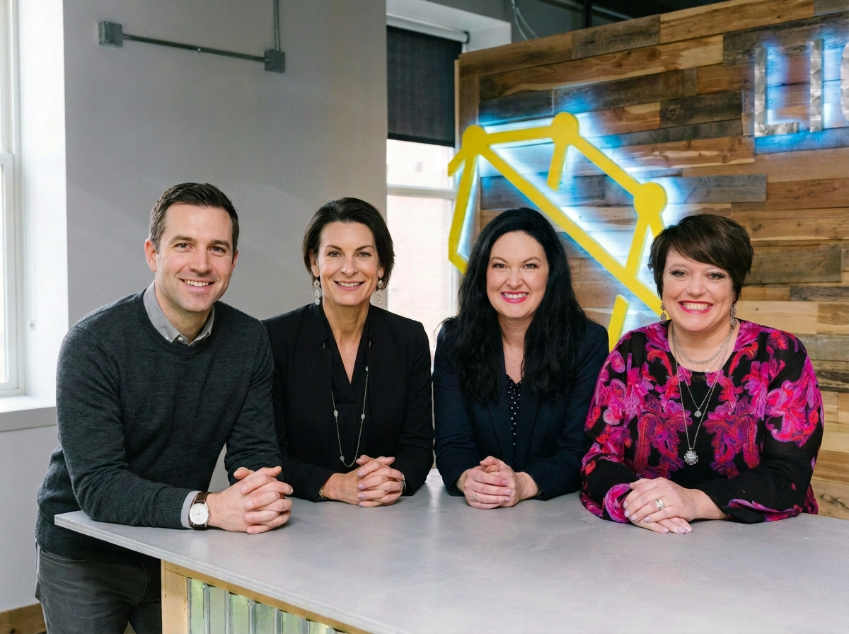 Four people sitting at a table, smiling, in a modern office space with wood and neon decor in the background.