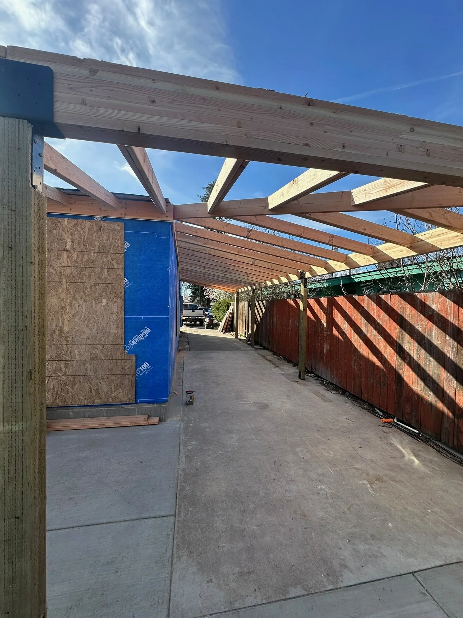 Construction site with wooden framework, plywood panel, and electrical wiring on concrete ground under a blue sky.