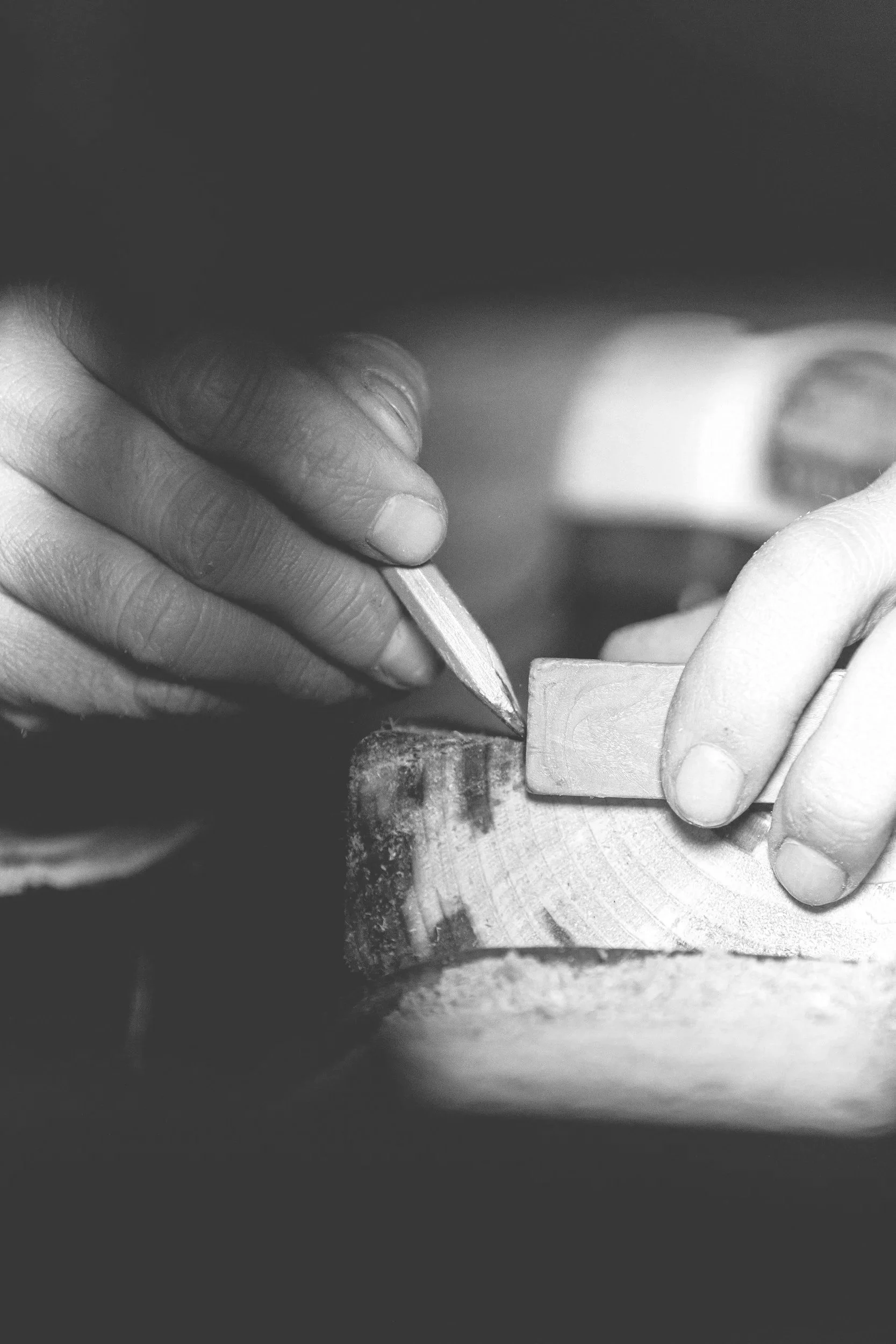 Close-up of hands using a chisel and hammer to carve a piece of wood.