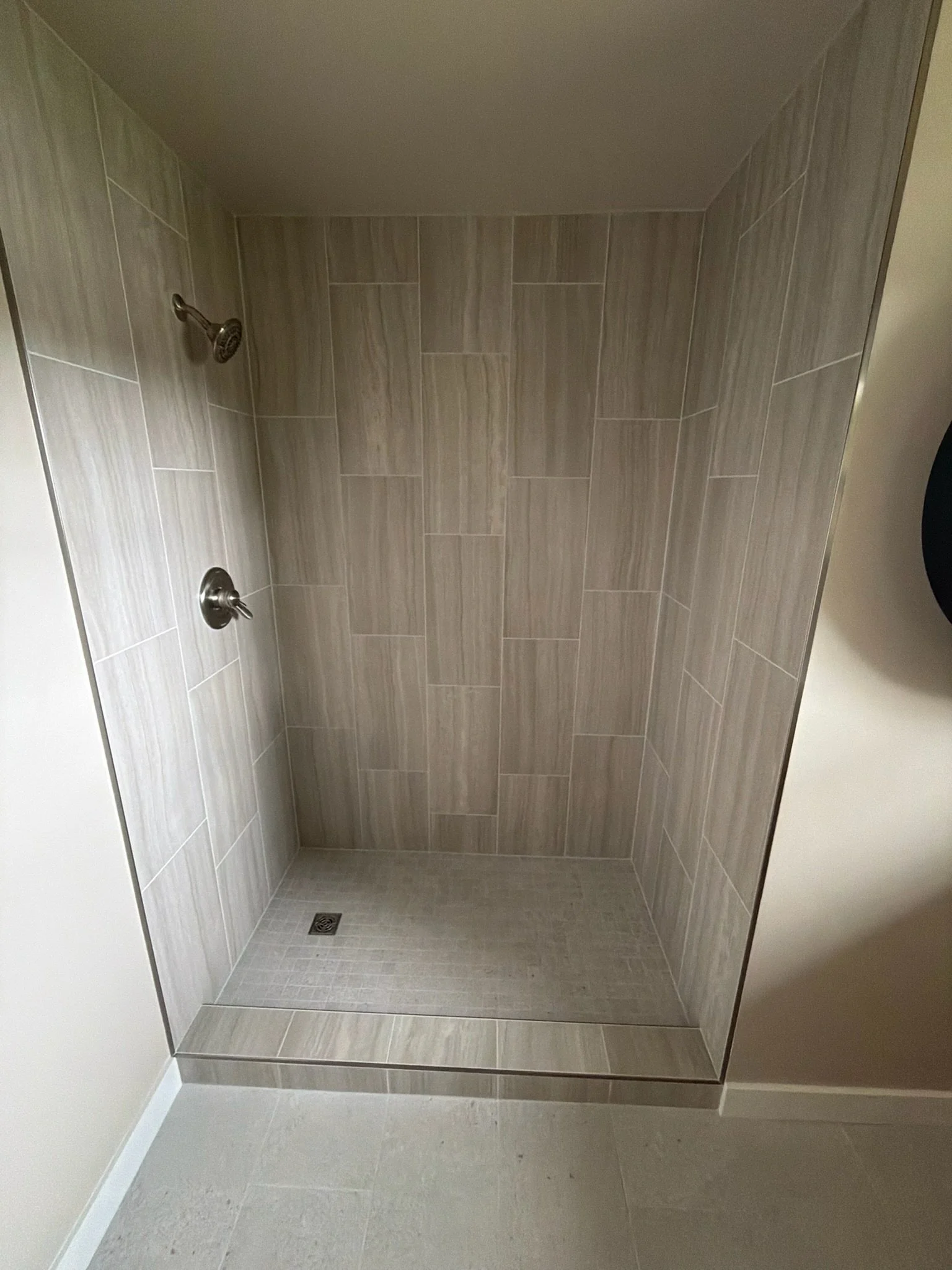 A tiled shower area with a shower head and a faucet, with light-colored tiles on the walls and floor.