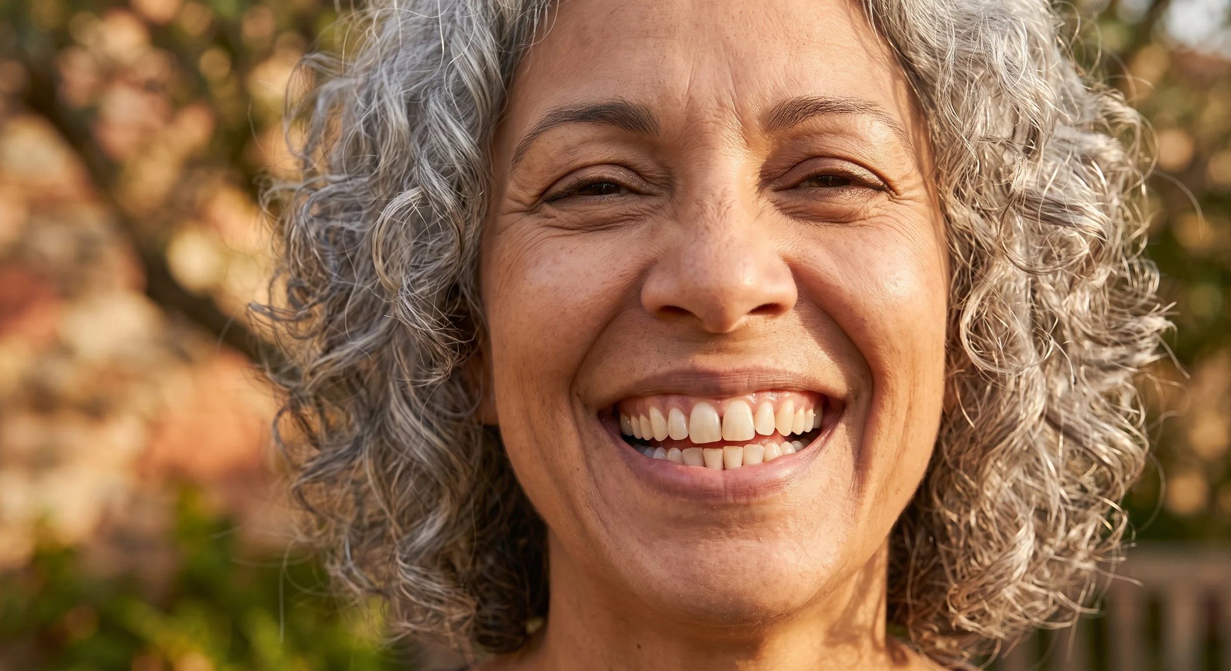 Close-up of a joyful middle-aged woman with curly gray hair smiling outdoors.
