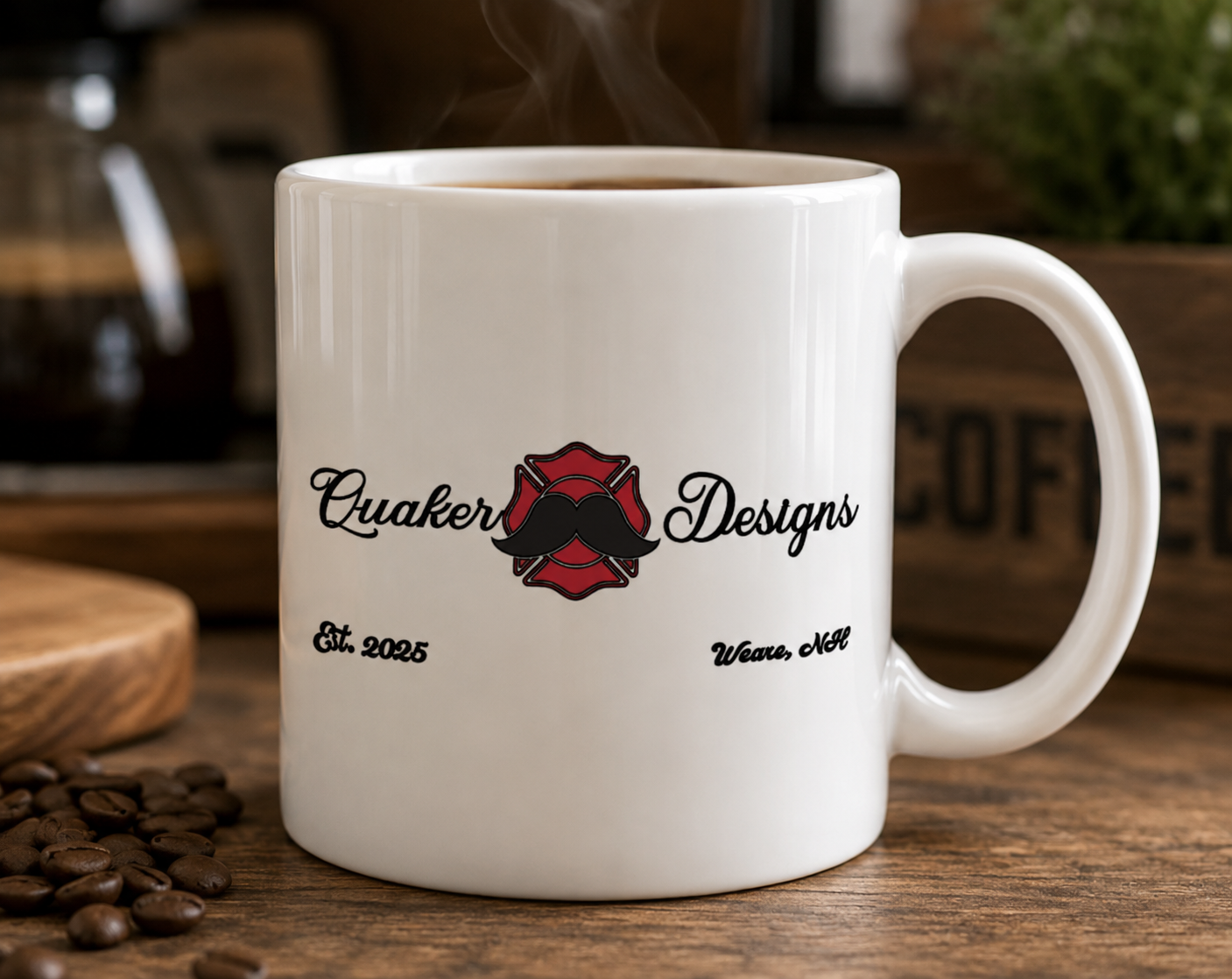 White coffee mug with a logo that says 'Quaker Designs' with a mustache graphic, on a wooden table with coffee beans nearby.