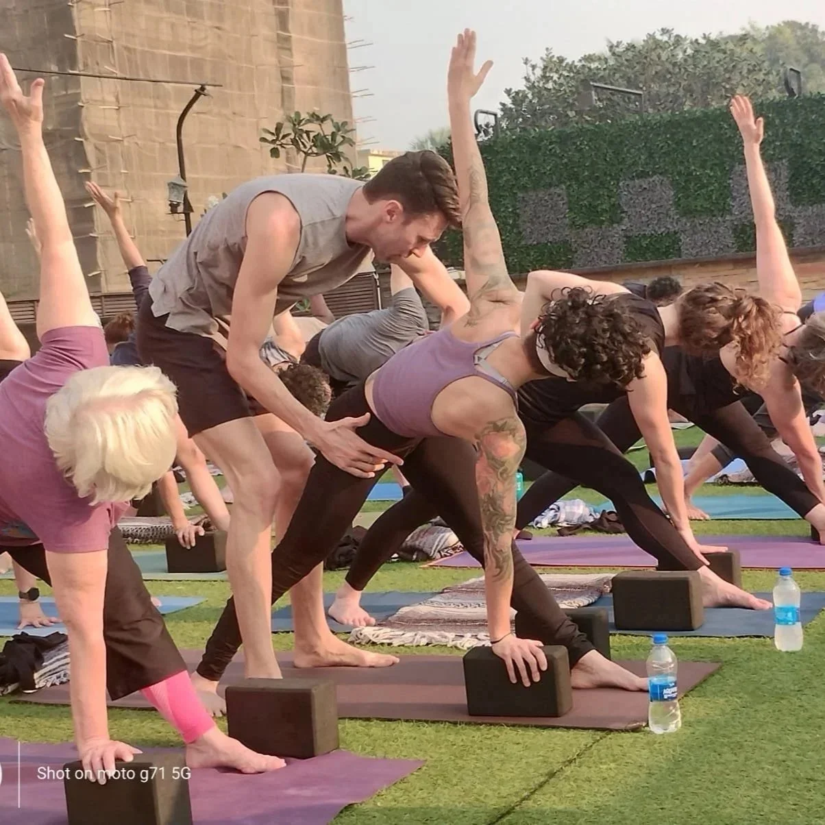 Free yoga class outdoors, with practitioners practicing yoga with instructor assisting a person
