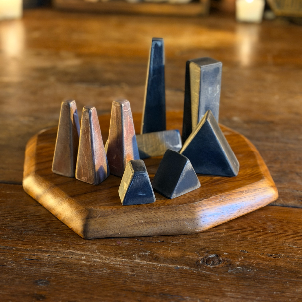 Set of dark wooden geometric obelisk pieces arranged on a hexagonal wood base, labeled ‘Bone Bells’”