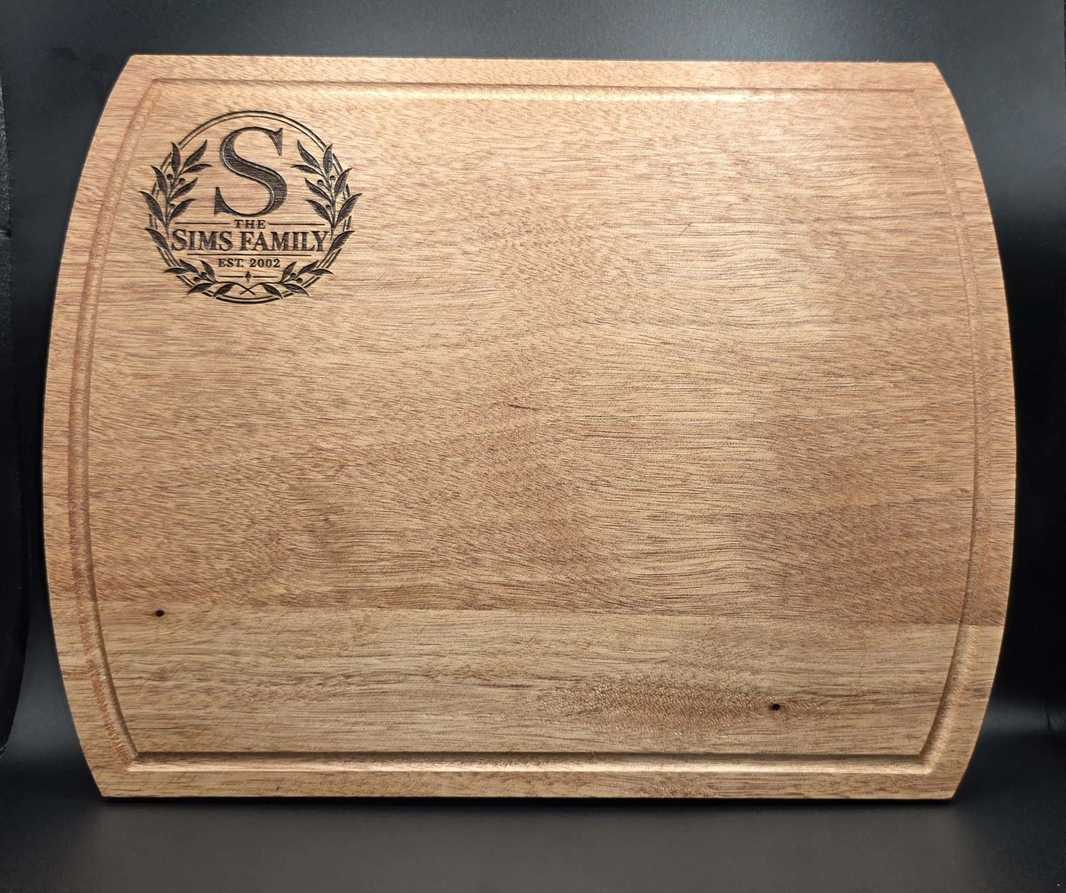 Personalized walnut cutting board with a laser-engraved Sims Family monogram and decorative wreath design.