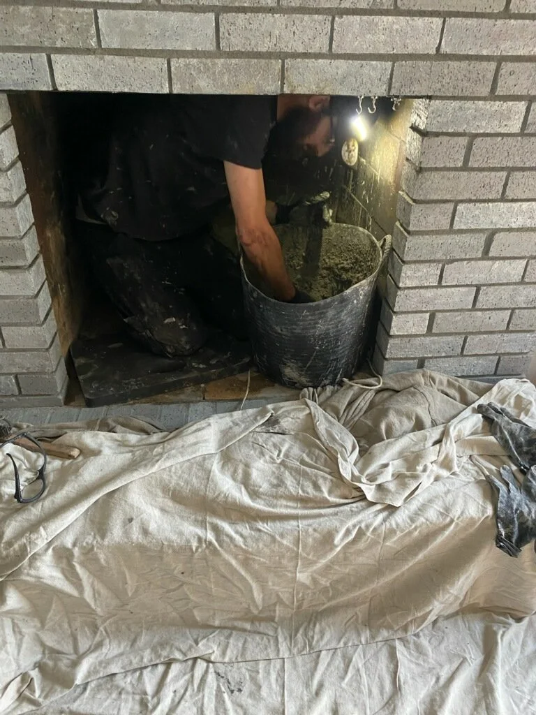 working inside a fireplace, installing/repairing ceramic wool, with a light focused on the work area and a drop cloth protecting the floor.