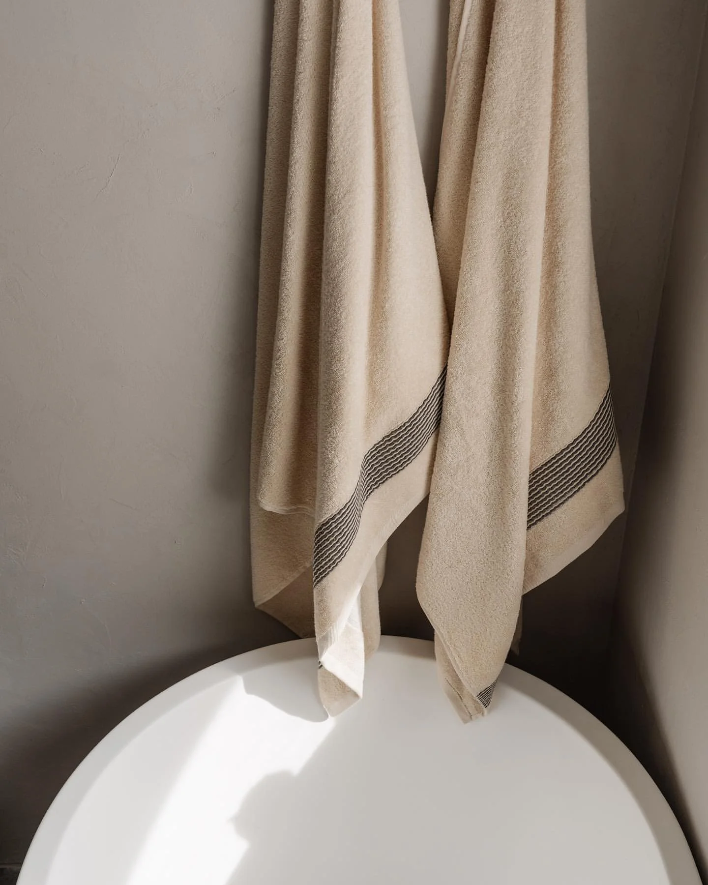 Micro cement walls with stone resin bath and ivory towels with stripe detail