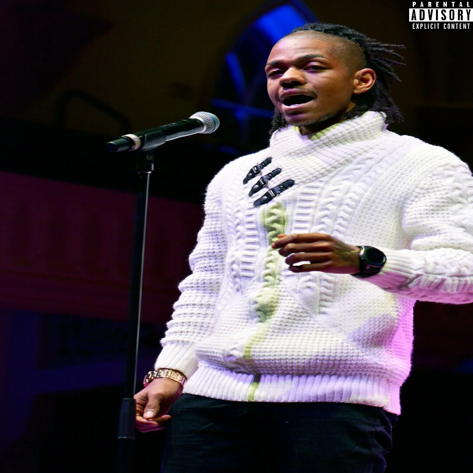 A person with braids and a white sweater speaking into a microphone on stage.