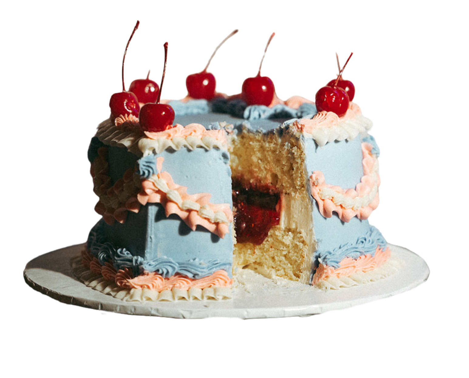 A decorated birthday cake with a slice removed, revealing yellow cake layers with red cherry filling inside. The cake is light blue with pink and white icing piping, topped with cherries and blueberries, and sits on a white round cake board.