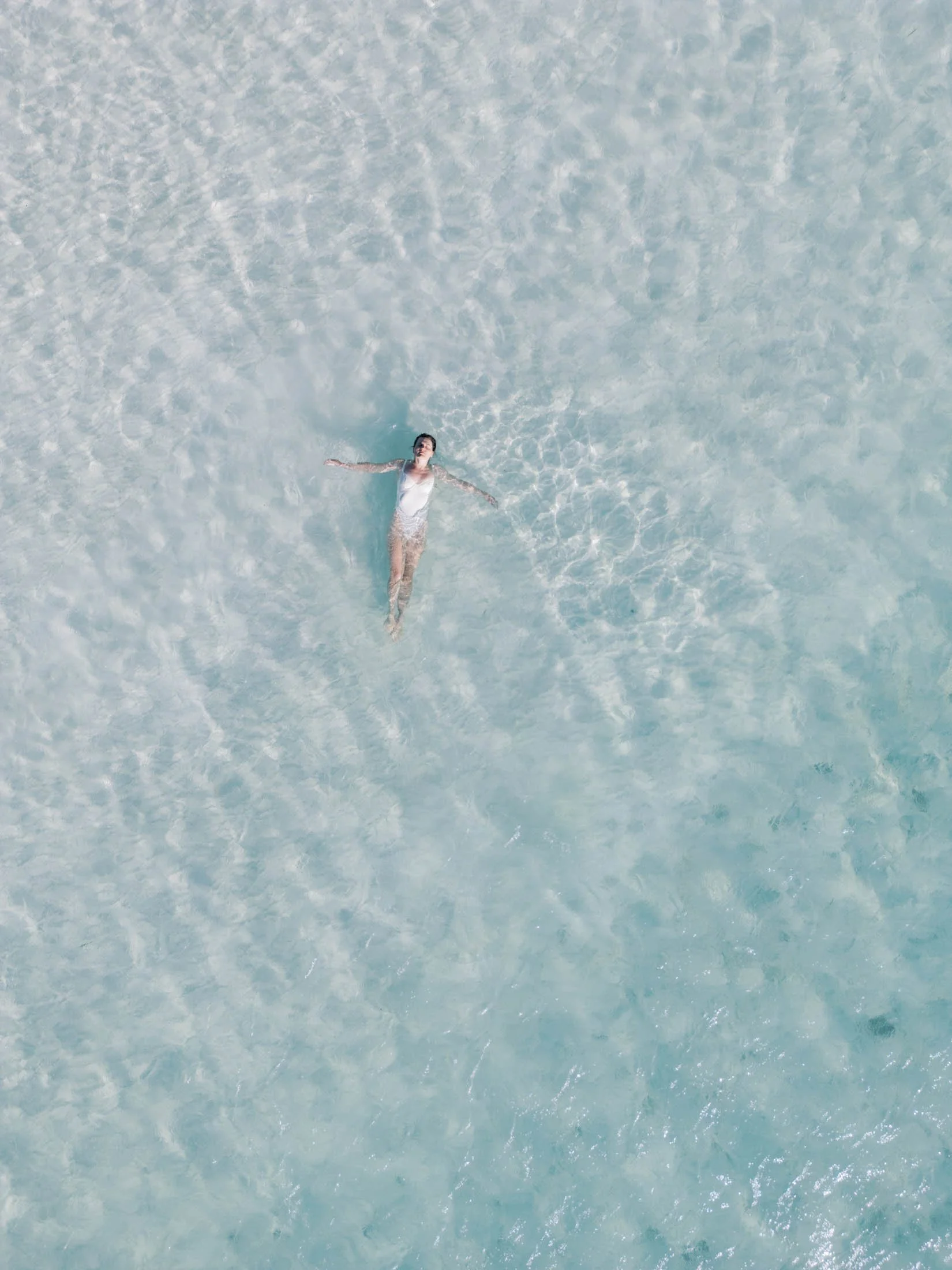 A person floating on their back in clear, shallow water.