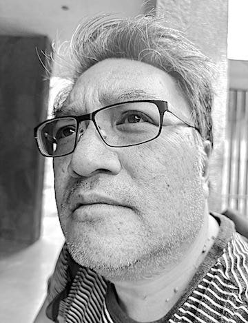 A black-and-white close-up of a middle-aged man with glasses and gray hair, looking slightly upward.