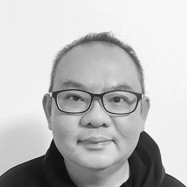 Close-up black and white portrait of a man with glasses smiling at the camera.