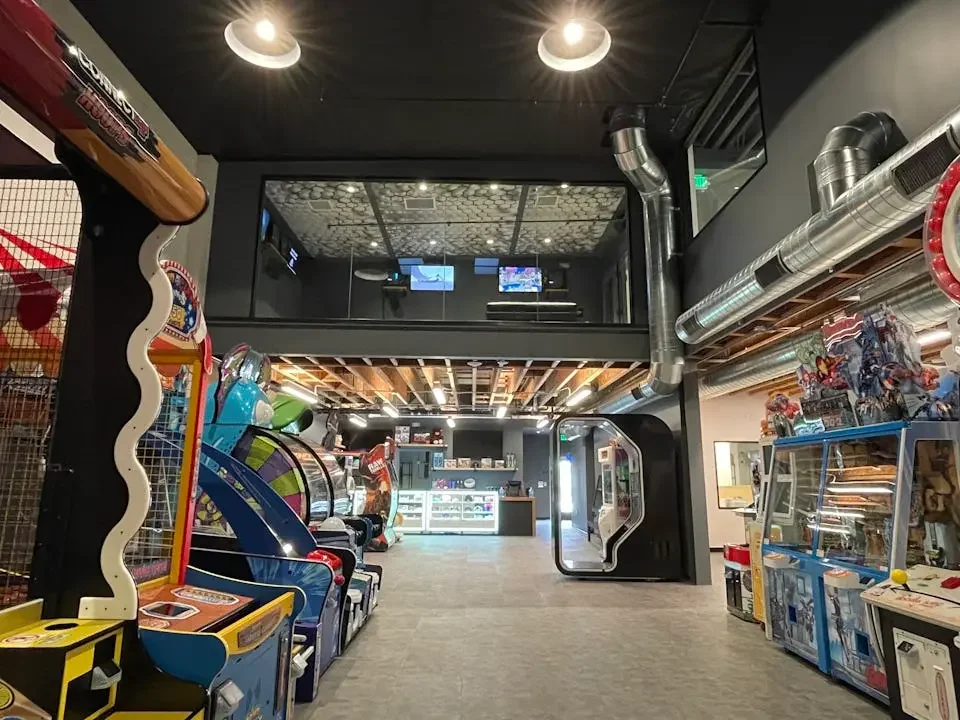 An arcade with various gaming machines, a snack counter, and a second-floor viewing area.