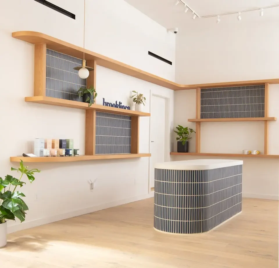 Modern interior with wooden shelves, potted plants, a tiled curved reception desk, and minimal decor.