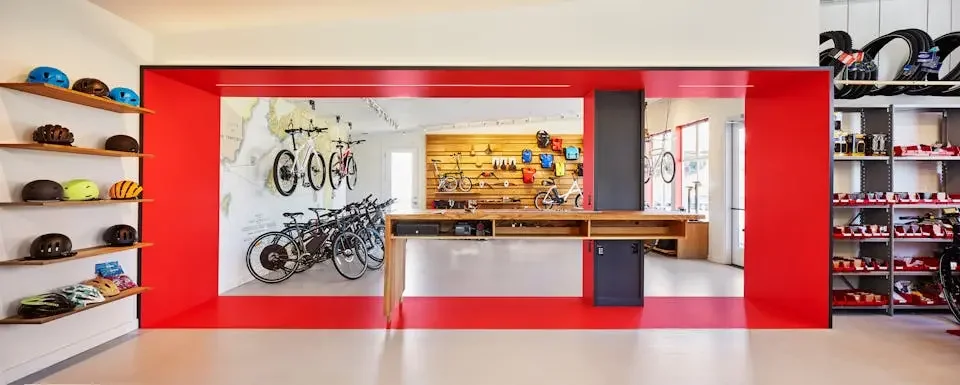 A bicycle shop with helmets on shelves on the left, bicycles on a wall and floor display in the back, and helmets on red, white, and black shelves on the right.